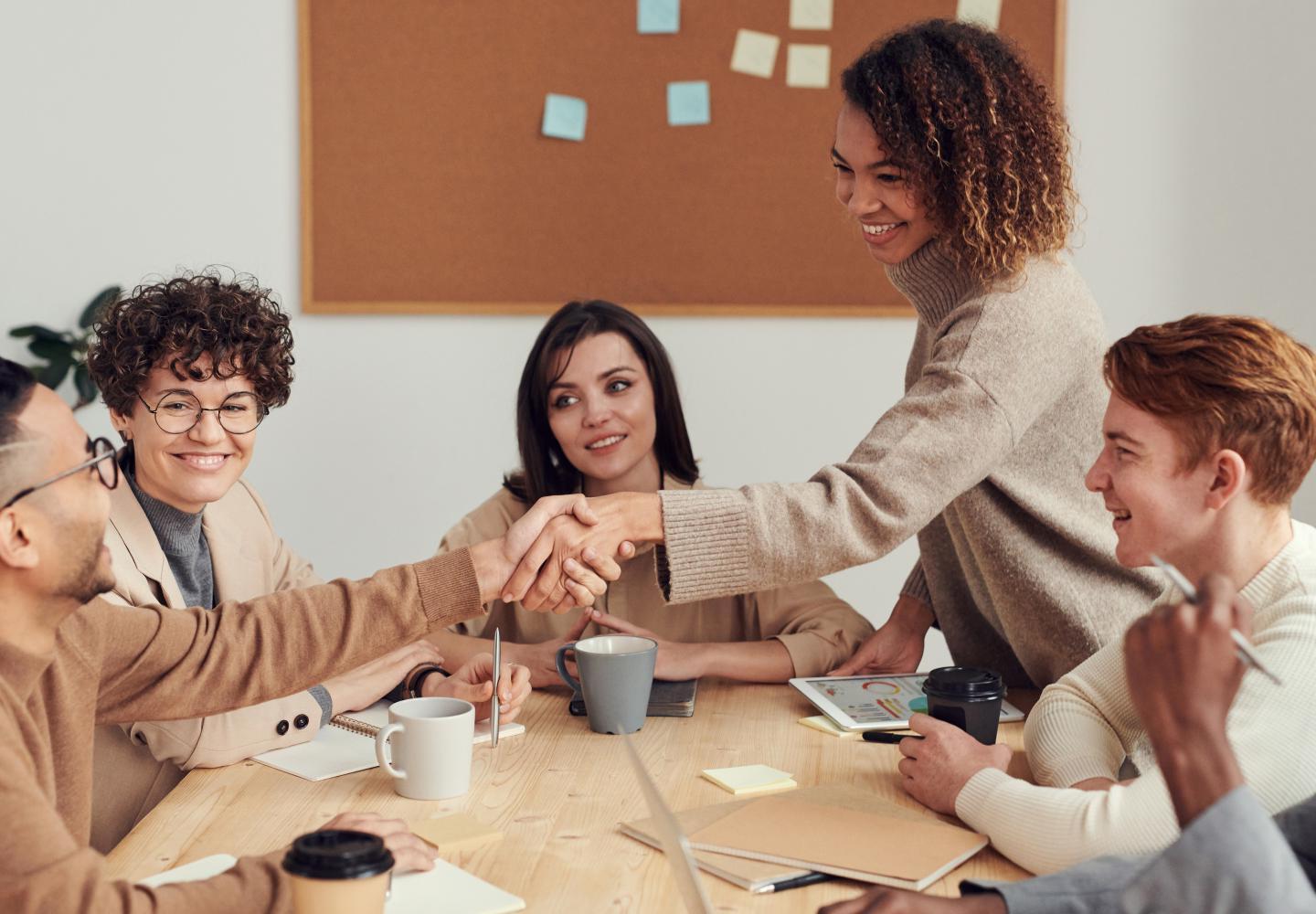 Woman shakes man's hand with group seated around table.